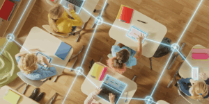overhead shot of students sitting at desks all on technology with lines connecting them to symbolize Ai