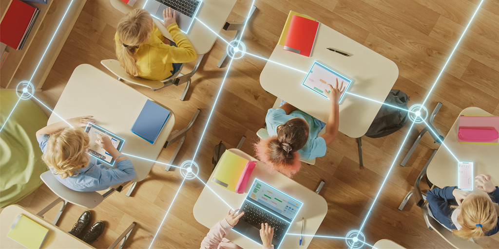 overhead shot of students sitting at desks all on technology with lines connecting them to symbolize Ai