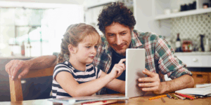 man and girl sitting at a table both staring at a tablet