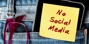 back pocket of jeans with a pair of red glassed and cell phone that has a sticky with "No Social Media" written on it