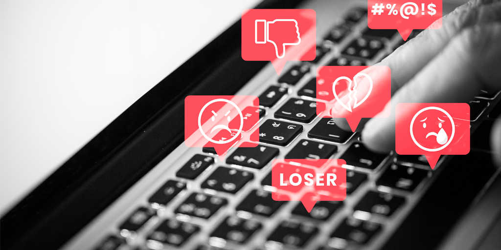 closeup of a computer keyboard with red speak bubbles with negative icons symbolizing cyberbullying