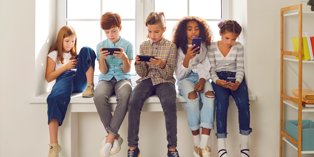 A diverse group of children sitting on a window sill all on devices